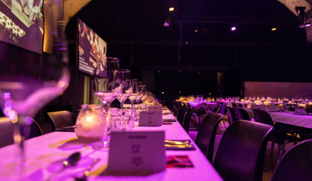 Een uitzicht van een lange tafel met glazen, bestek en lichten in een sfeervolle zaal.