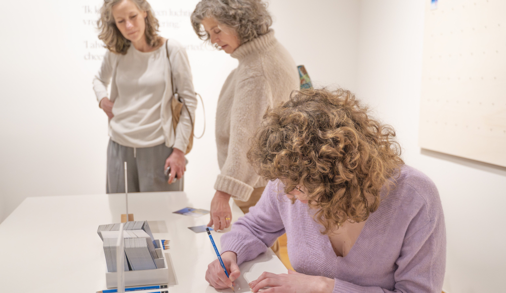 Drie vrouwen bekijken en schrijven in een kunstexpositie.