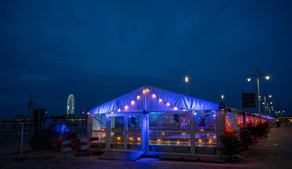 Ein beleuchtetes Strandzelt mit blauen und anderen Lichtern an der Küste von Scheveningen bei Nacht.