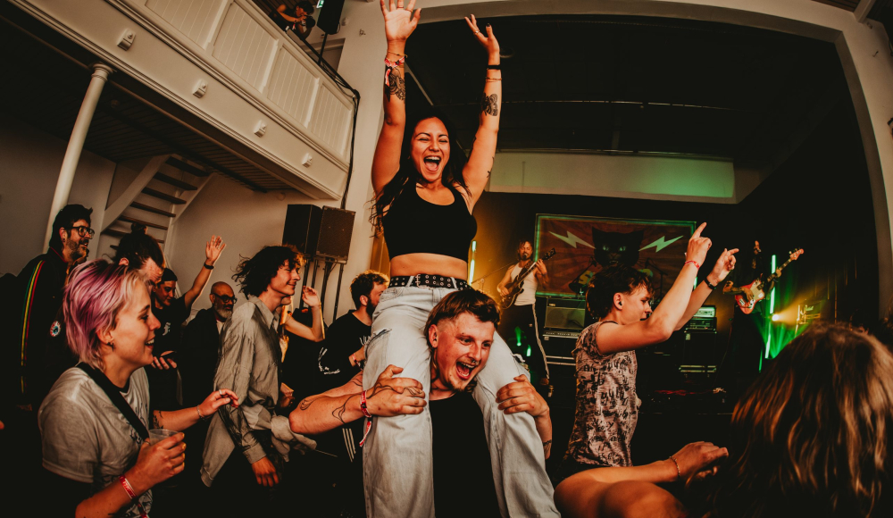 Feestende mensen tijdens concert. Een vrouw zit op de schouders van een man in een drukke zaal