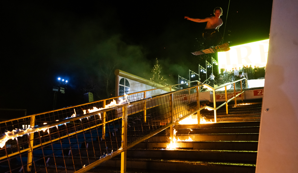 Événement de snowboard nocturne. Un snowboardeur saute par-dessus une clôture en feu.