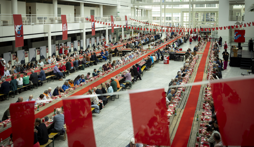 Mensen zitten samen aan lange tafels voor een maaltijd.