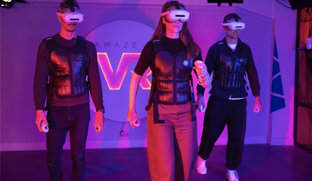 Amaze VR. Drei Personen mit VR-Headsets und Westen in einem Spielort.