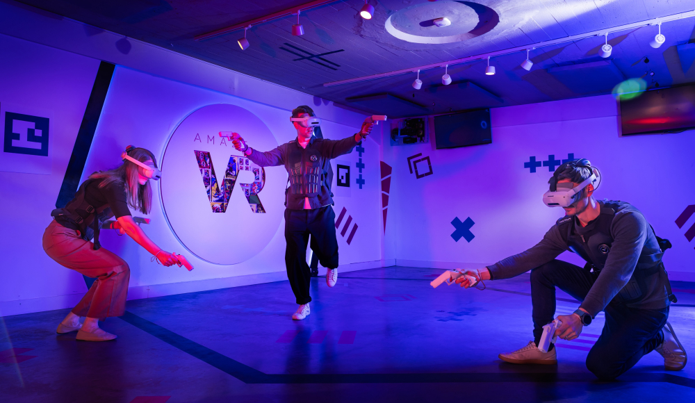 Amaze VR Shooter Running. Drei Personen spielen ein Virtual-Reality-Spiel in einem bunten Raum.