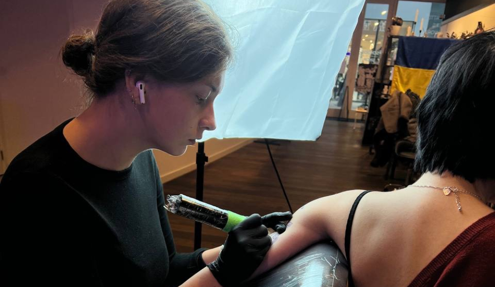 A tattoo artist is tattooing a client's arm.