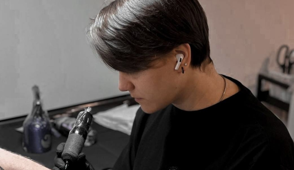 A tattoo artist is tattooing an arm with a machine.