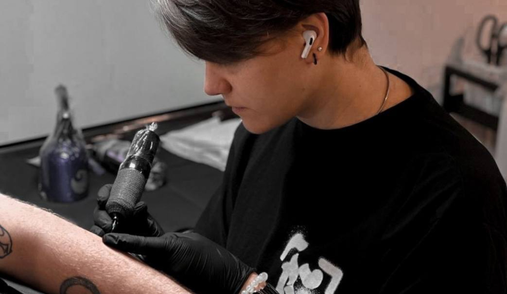 A tattoo artist is tattooing an arm with a tattoo machine.