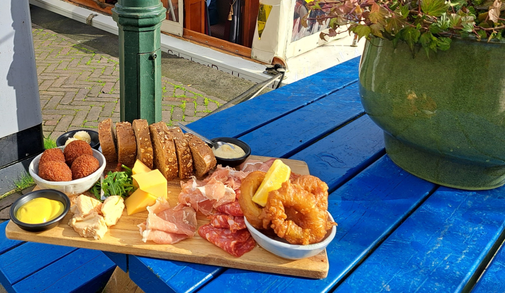 Tafel met een ontbijtplank met op de achtergrond de boot van de Willemsvaart