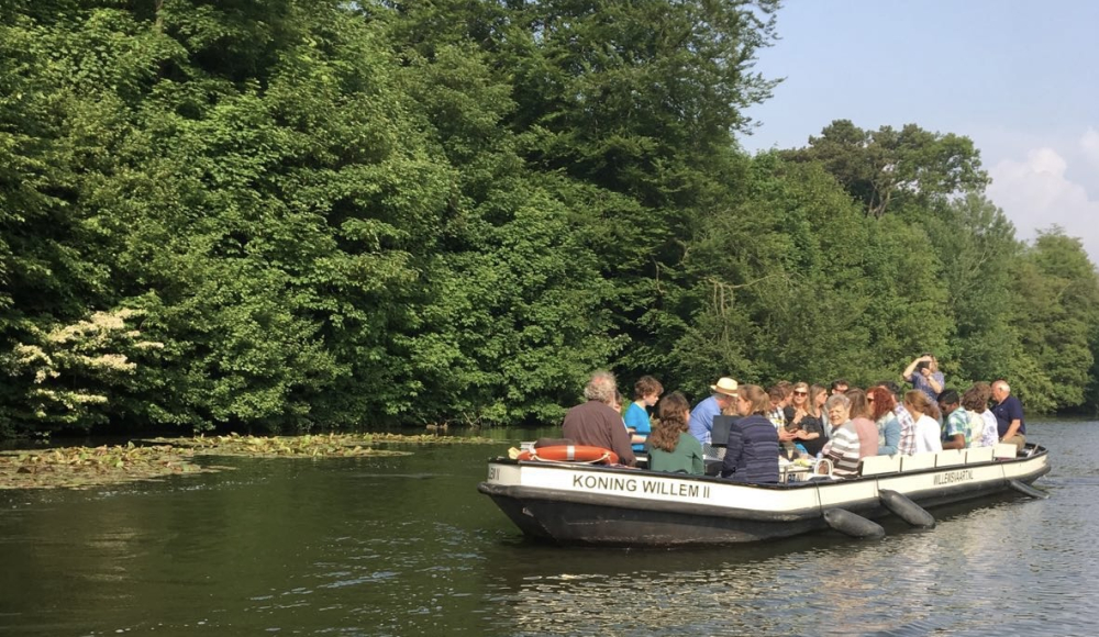 Een boot van de Willemsvaart die over de Haagse gracht vaart met op de achtergrond groene bomen