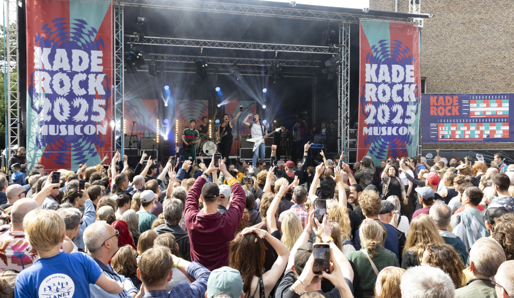 A crowded festival with a stage and an audience dancing.