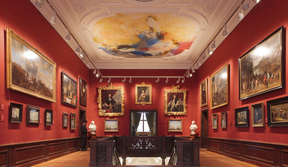 Historische interieur van het Mauritshuis met schilderijen aan de muren en een trap in het midden. Historische interieur van het Mauritshuis met schilderijen aan de muren en een trap in het midden.