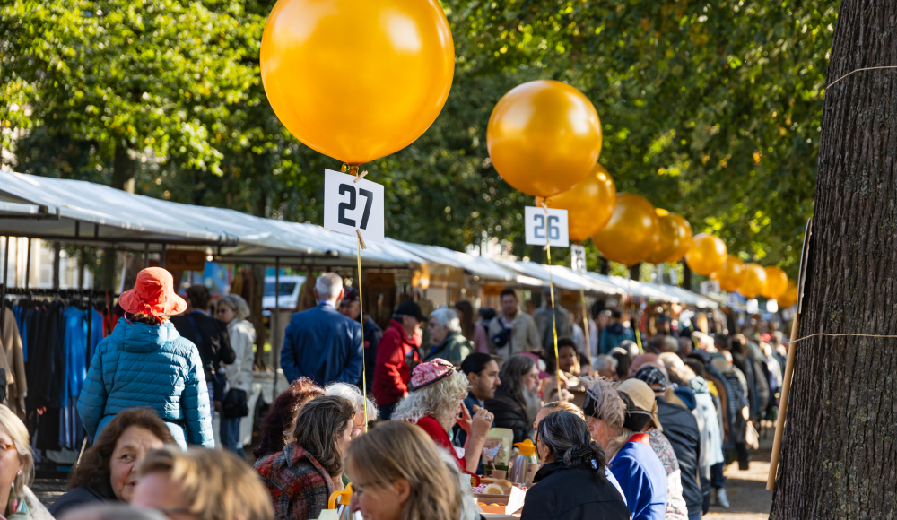 Een drukke markt met mensen en gele ballonnen in Den Haag.