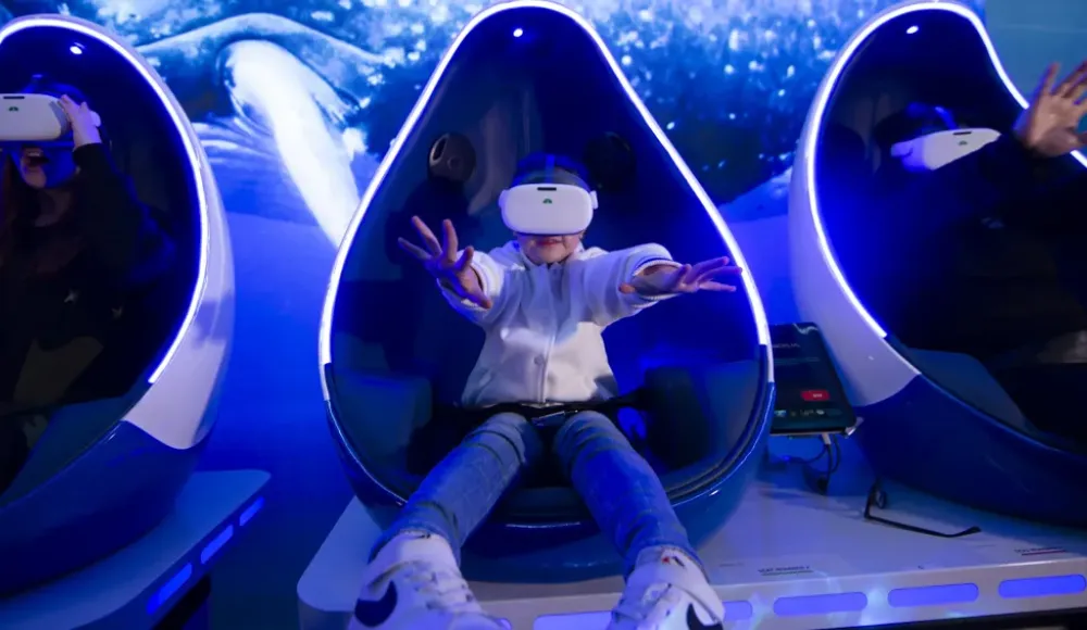 Een kind en twee volwassenen dragen VR-brillen in stoelen.