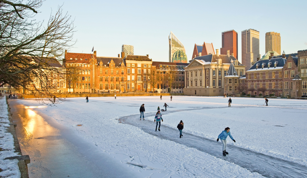 Mensen aan het schaatsen op de bevroren Hofvijver in Den Haag met de moderne skyline op de achtergrond
