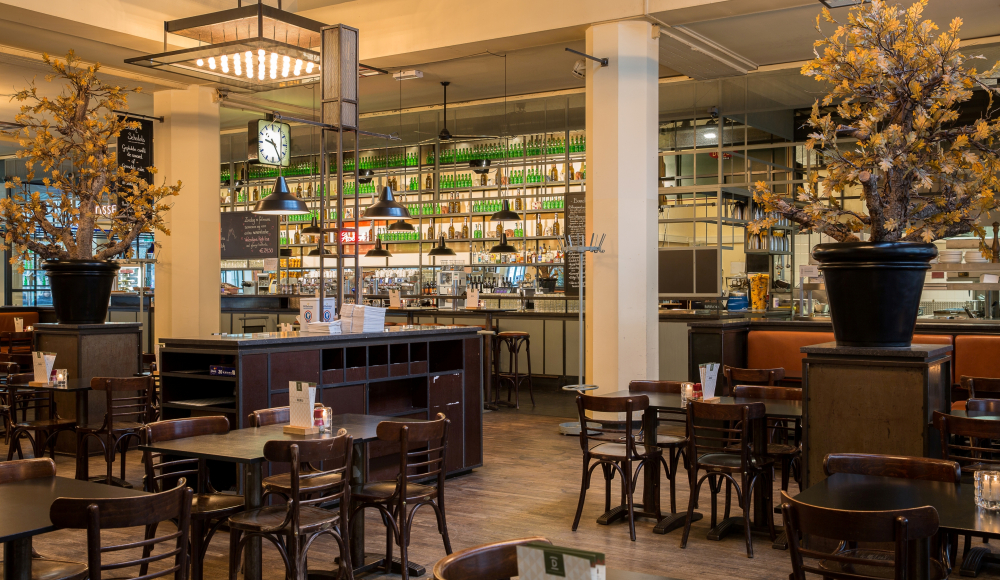 Industriele interieur van grand café Dudok met zich op de bar en lege houten stoelen en tafeltjes.