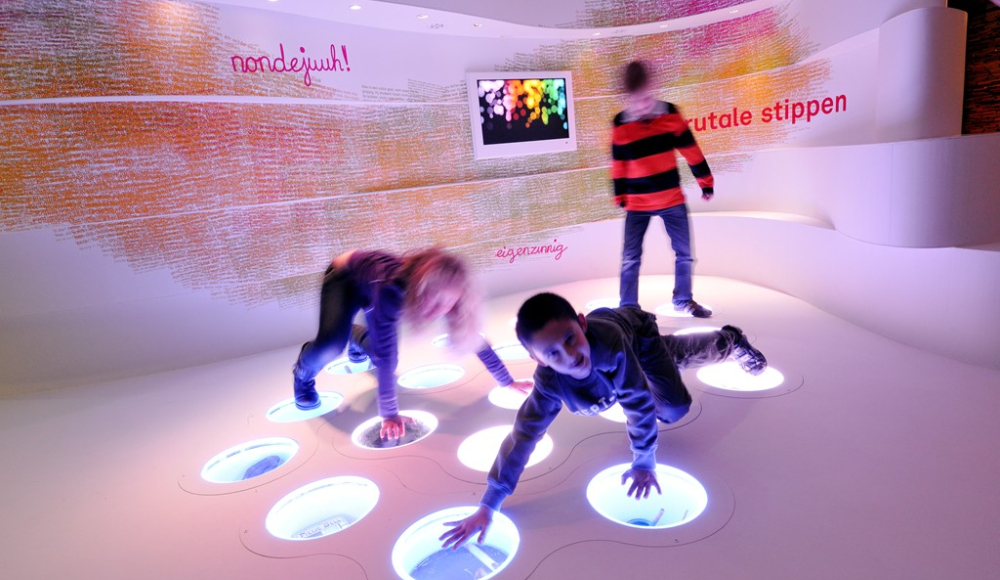 Kinderen die op met hun handen en voeten op stippen staan bij het Stippenspel in het Kinderboekenmuseum