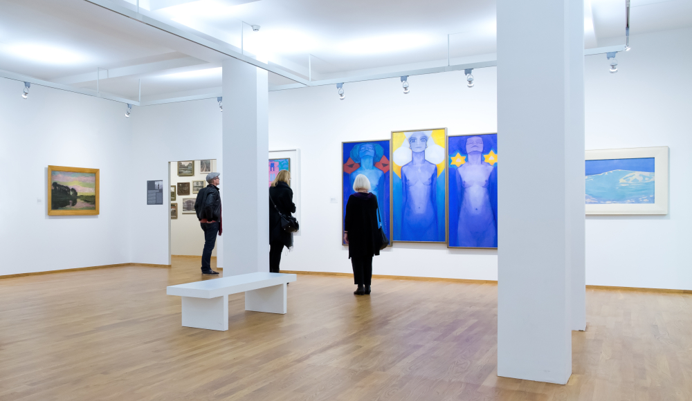 Een lichte witte ruimte in Kunstmuseum Den Haag waar mensen naar kunst kijken waaronder werk van Mondriaan Een lichte witte ruimte in Kunstmuseum Den Haag waar mensen naar kunst kijken waaronder werk van Mondriaan