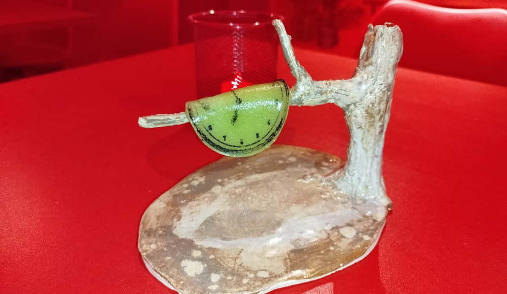 Une décoration en fruits verts suspendue à une branche sur un plateau en bois.