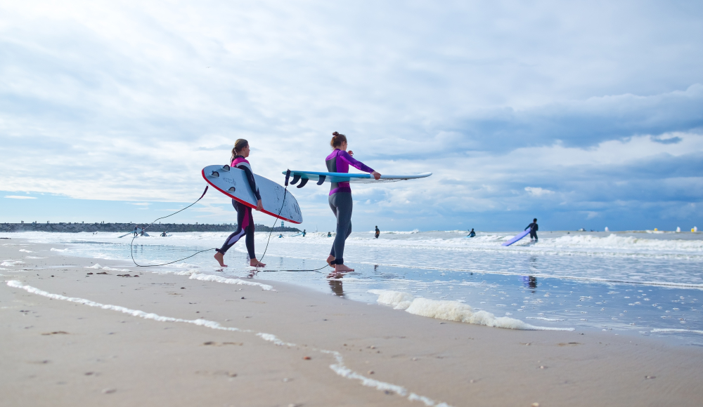 Twee surfers met surfboards onder hun arm in de branding op Scheveningen strand Twee surfers met surfboards onder hun arm in de branding op Scheveningen strand