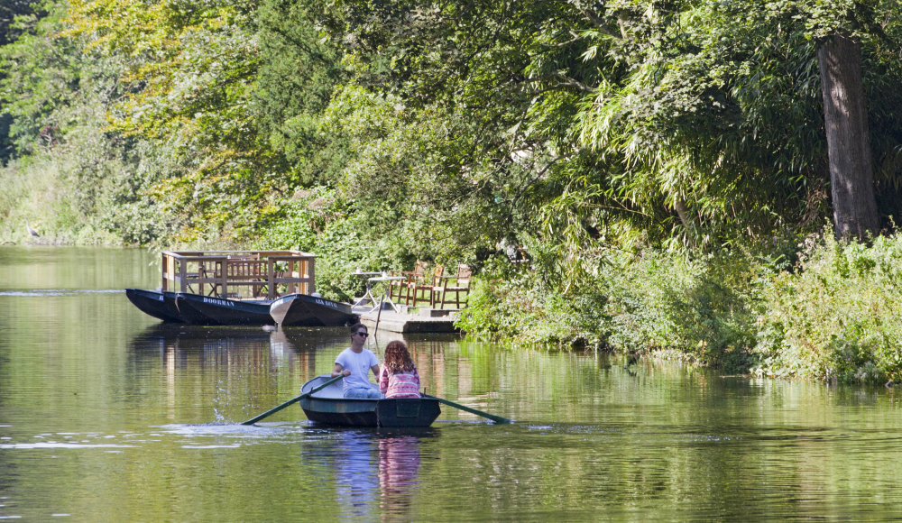 Een man en vrouw varend in een roeibootje door het groene Westbroekpark