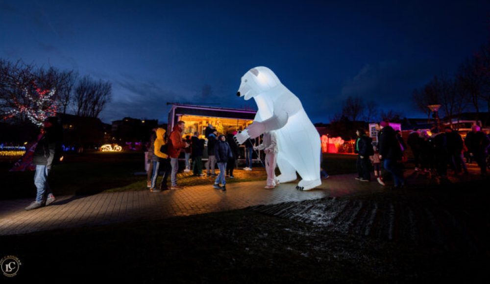 Ein großer, beleuchteter Eisbär steht zwischen Menschen.