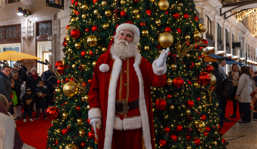 Kerstman in een rode outfit met een kerstboom vol decoraties.