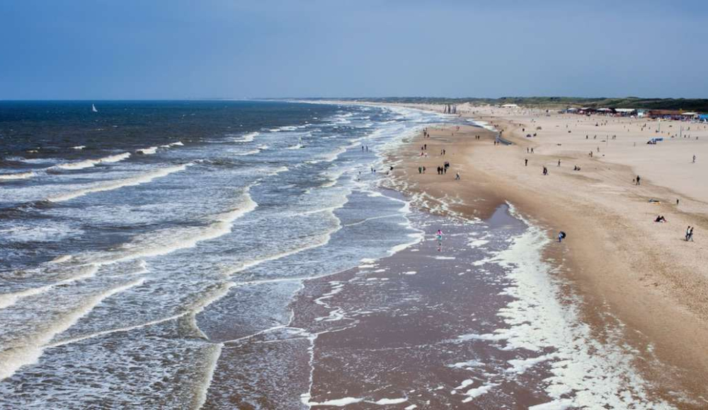Kustlijn van Den Haag van onder naar boven gefotografeerd. Je ziet een deel strand en de branding. 