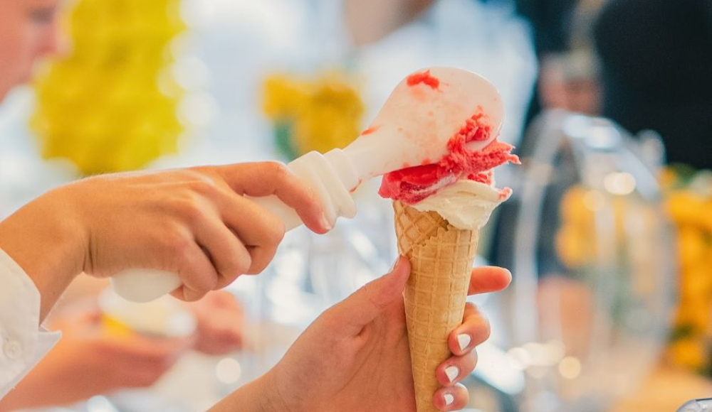 Een hand schept ijs in een hoorntje.