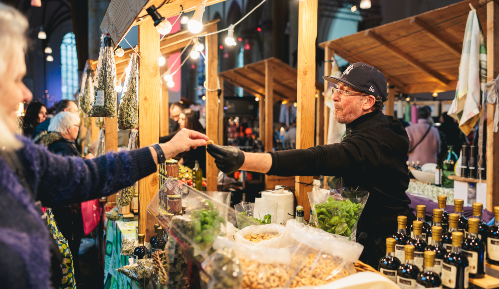 Kramer overhandigt iets aan een klant op de markt.