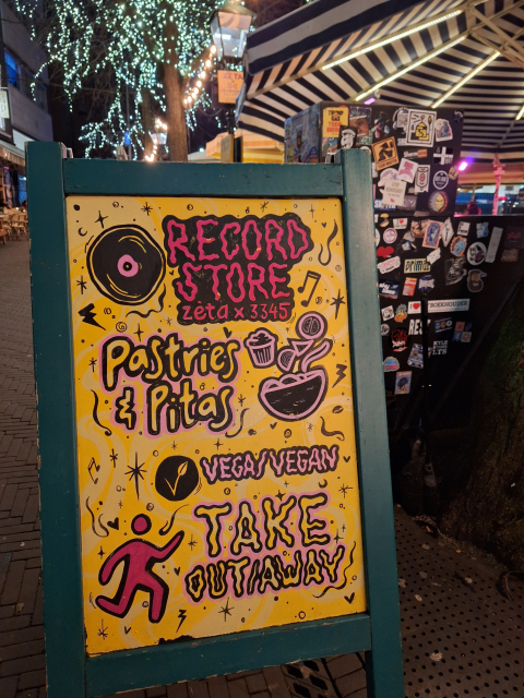 Zeta Krijtbord met informatie over een platenwinkel met veganistische afhaalopties.