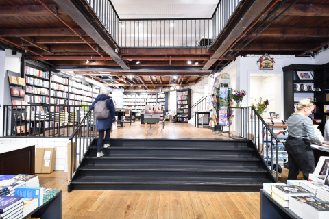 Interieur van boekwinkel De Vries Van Stockum met trap naar tafels en rekken vol boeken.