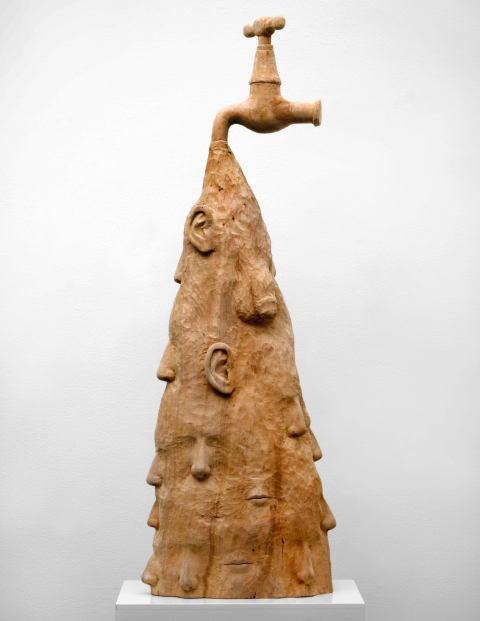 Une sculpture avec plusieurs visages humains et un robinet au sommet.