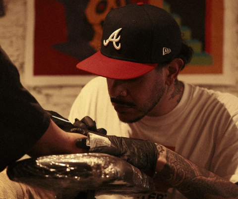 Een man met een cap zet een tattoo in een studio.