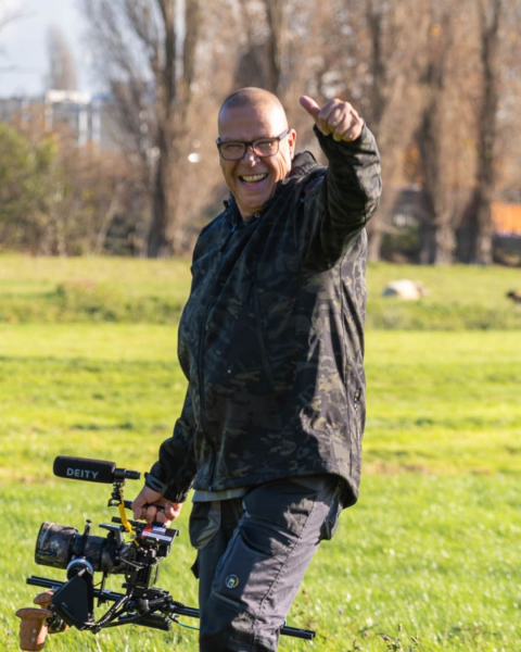 Een man lacht en geeft een duim omhoog terwijl hij een camera vasthoudt. Foto: Jaap Brand