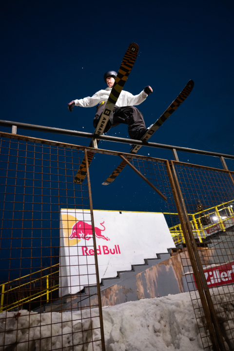 Skieur effectue un saut par-dessus une barrière avec de la neige en arrière-plan.