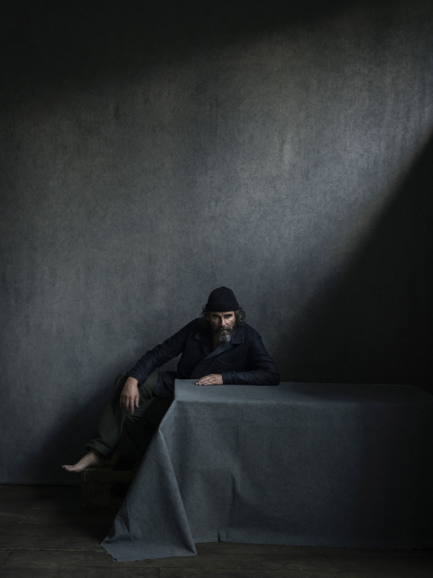 Een man in een donkere ruimte leunt op een tafel.