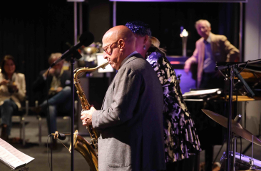Jazzmuzikant speelt saxofoon op een podium met publiek en medemuzikanten