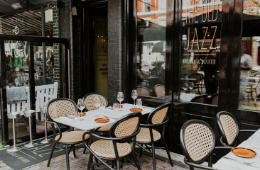 Een sfeervol terras bij Old Jazz, met gedekte tafels, rieten stoelen en een uitnodigende uitstraling, perfect voor een gezellige eetervaring.