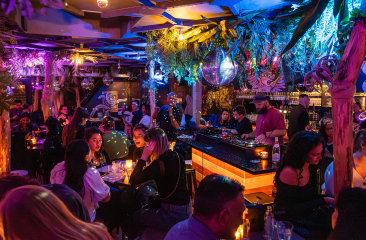 De foto toont een levendige en sfeervolle bar met een tropisch en modern interieur. De foto toont een levendige en sfeervolle bar met een tropisch en modern interieur.