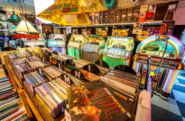 Retro muziek- en platenwinkel met vinylbakken, kleurrijke jukeboxen en vintage muziek, waaronder Elvis Presley-platen en gouden records.