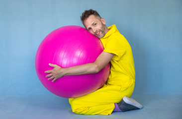 Promotiebeeld voor Peutervoorstelling Rokkerol Efrem Stein zit op de grond in een gele overal en knuffelt een grote roze bal 