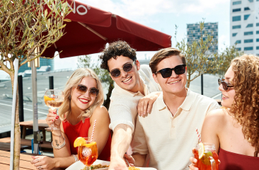 Vier vrienden genieten van pizza en cocktails op een zonnig stads terras.