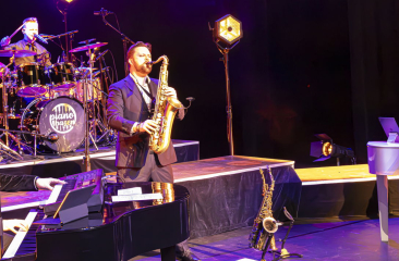De leden van de Pianobazen staan op het podium met hun instrumenten.
