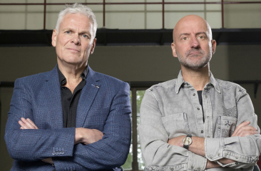Joep van Deudekom en Rob Urgert poseren naast elkaar met een serieuze blik en hun armen over elkaar. 