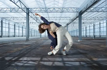 danser in een moderne pose in een lege, glazen kas met stalen constructie