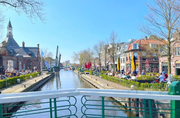 Zonnige dag bij de sluis van Leidschendam met volle terrassen, historische panden en blauwe lucht aan het water.