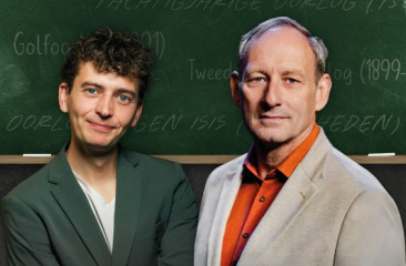 Twee mannen voor een schoolbord met historische termen, beiden kijken recht in de camera