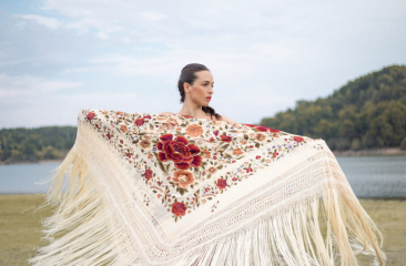 Foto in een Mediterrane omgeving met een meer en berg op de achtergrond waarin flamencodanseres Marina Paje met een mooie omslagdoek met opengestrekte armen staat.