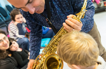 Een peuter kijkt naar de saxofoon van een muzikant tijdens het Ukkieconcert in Theater de Regentes