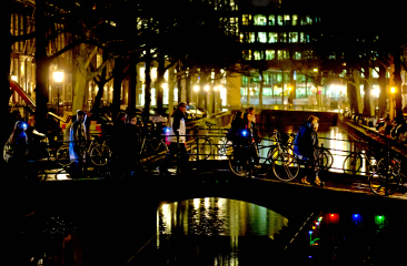 Wandelaars met lichtjes steken ’s avonds een brug over in een verlichte stad